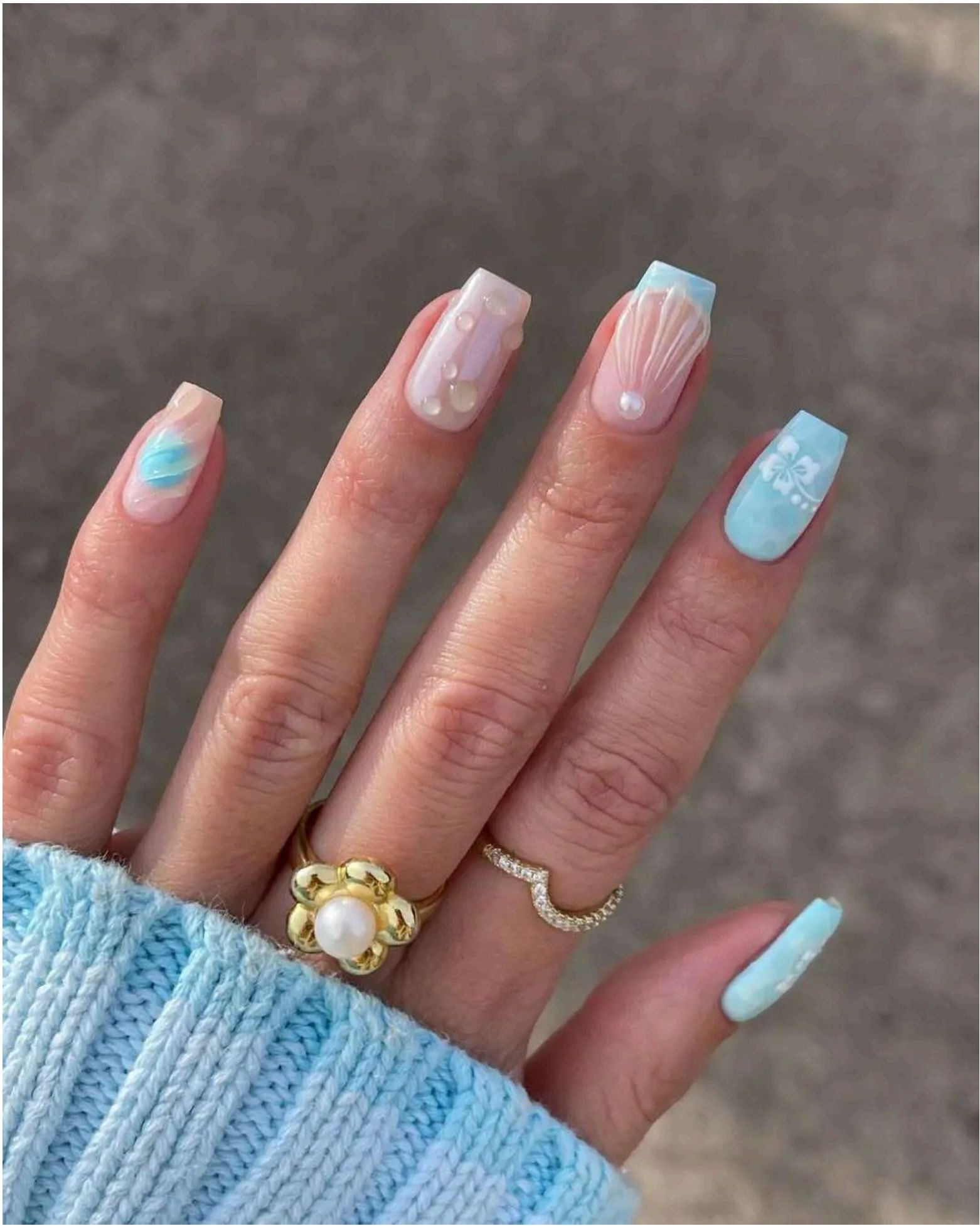 Mix of baby blue and sheer pink nails featuring seashells, pearls, and hibiscus flowers – straight out of a mermaid's manicure collection.