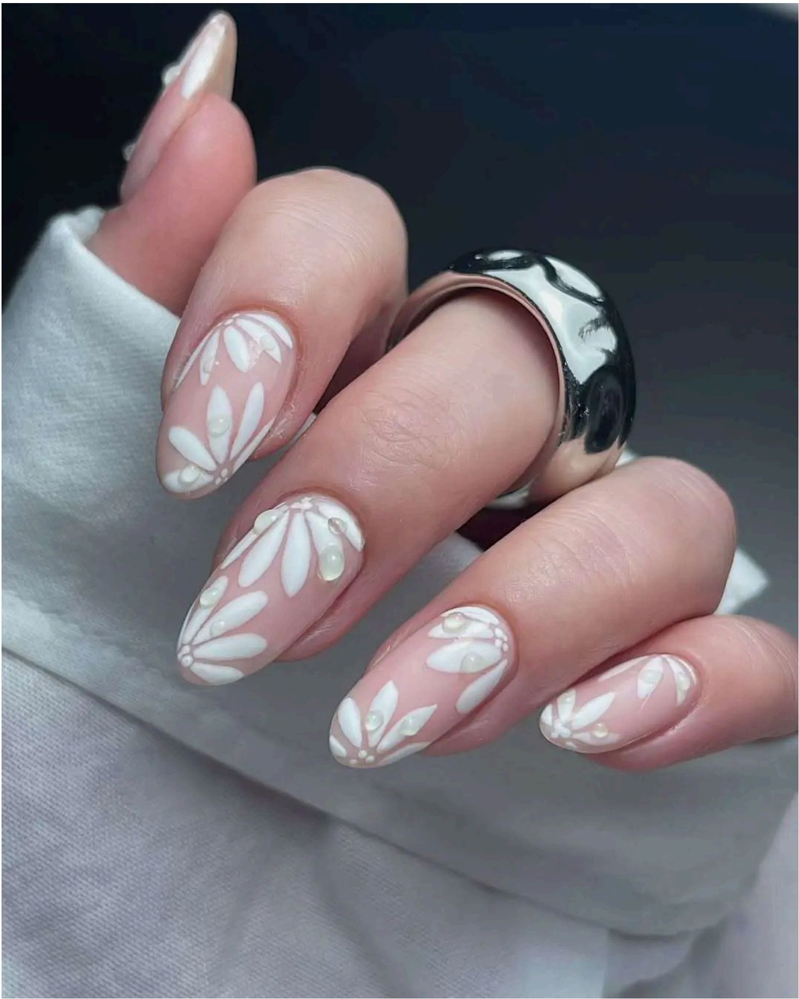 Nude almond nails with delicate white daisy designs and pearl accents create the perfect beachy-boho vibe.