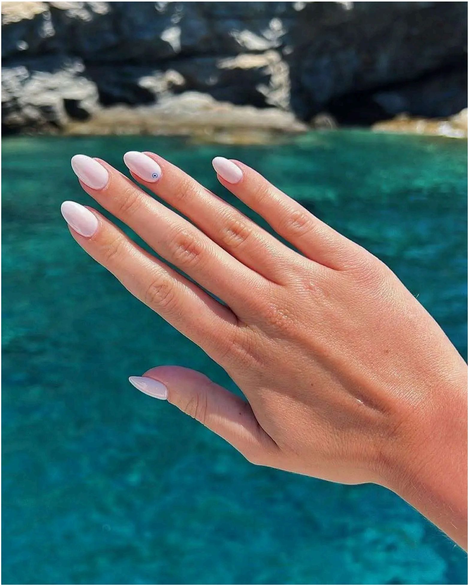 Milky white almond nails with a delicate blue evil eye accent – the perfect charm for beach days.
